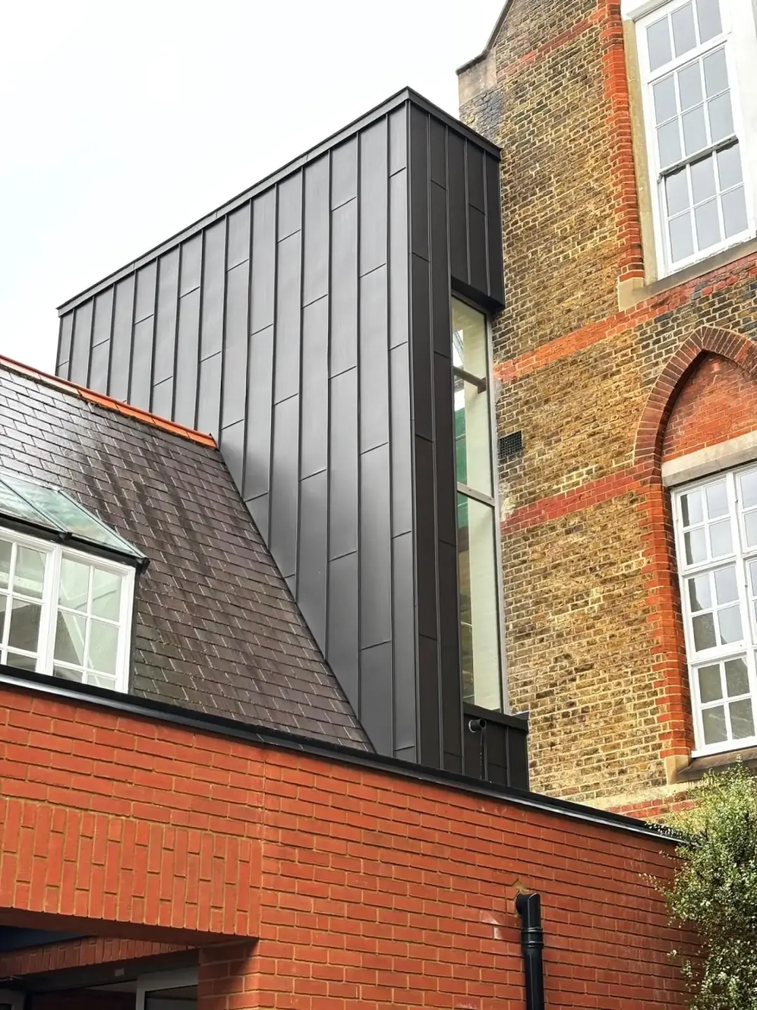 Tall dark standing seam zinc cladding beside a brick building in Fulham